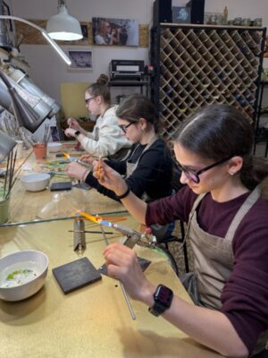 Участницы создают стеклянные бусины у горелок в мастерской GlassBaker