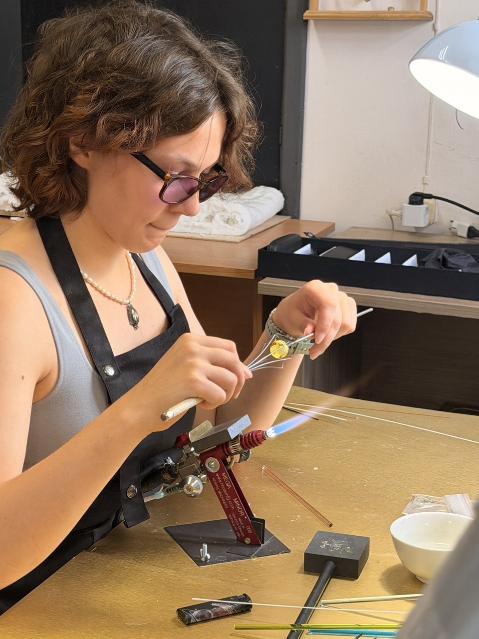 Участница формует полую стеклянную бусину у горелки на курсе GlassBaker